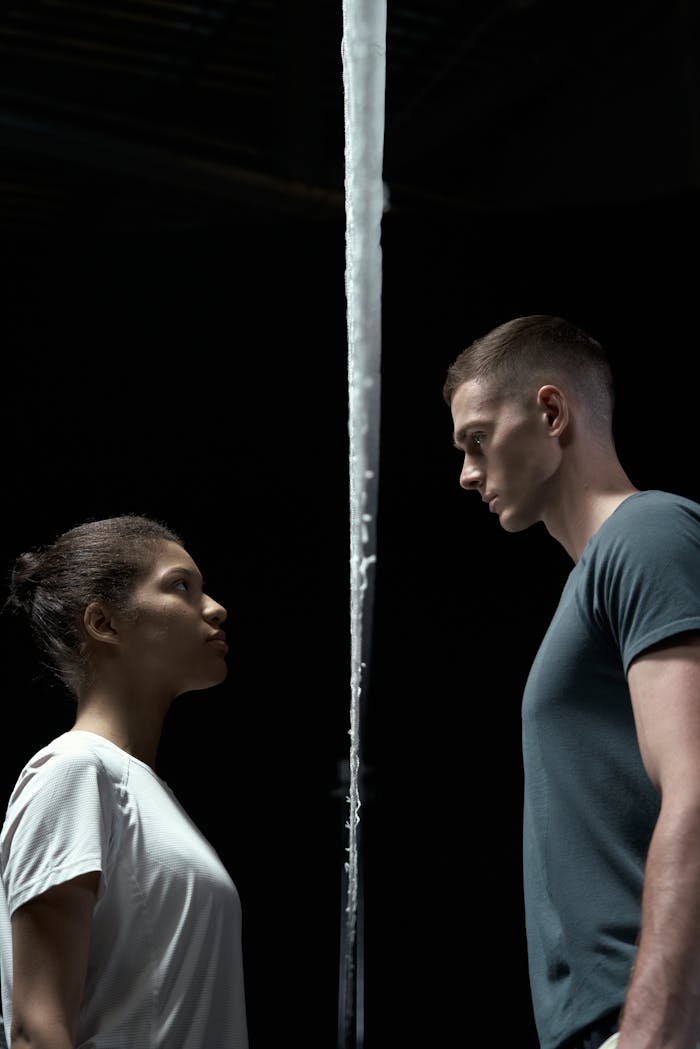 A dramatic portrait of a couple facing each other with a strong, serious gaze in a studio setting.
