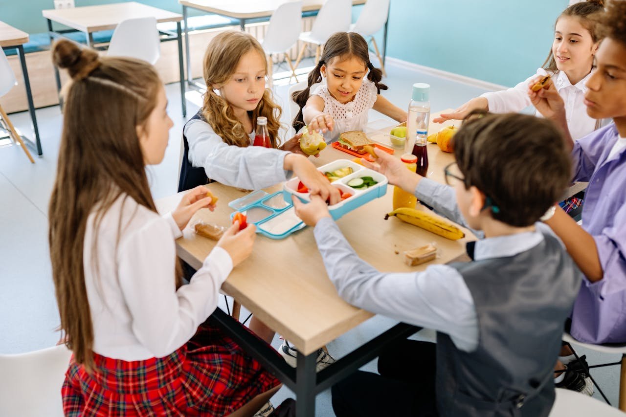 Group of diverse children having lunch in a school canteen, sharing and enjoying healthy snacks.